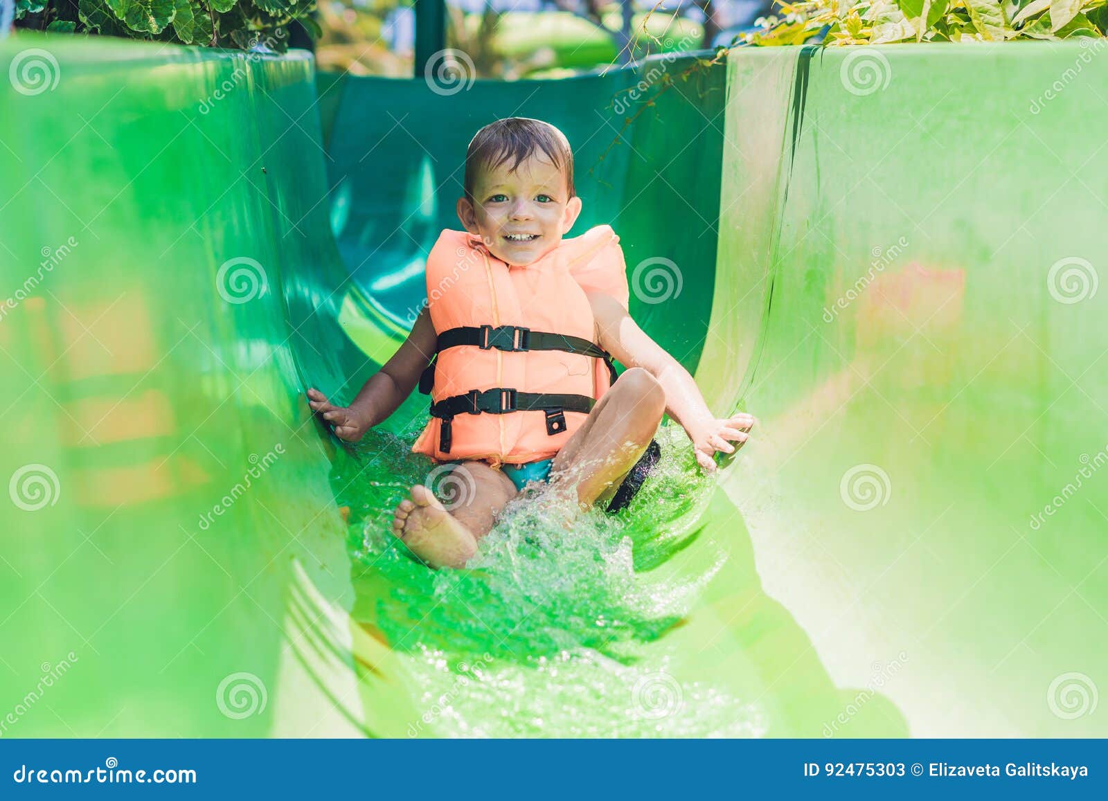 A Boy in a Life Jacket Slides Down from a Slide in a Water Park Stock