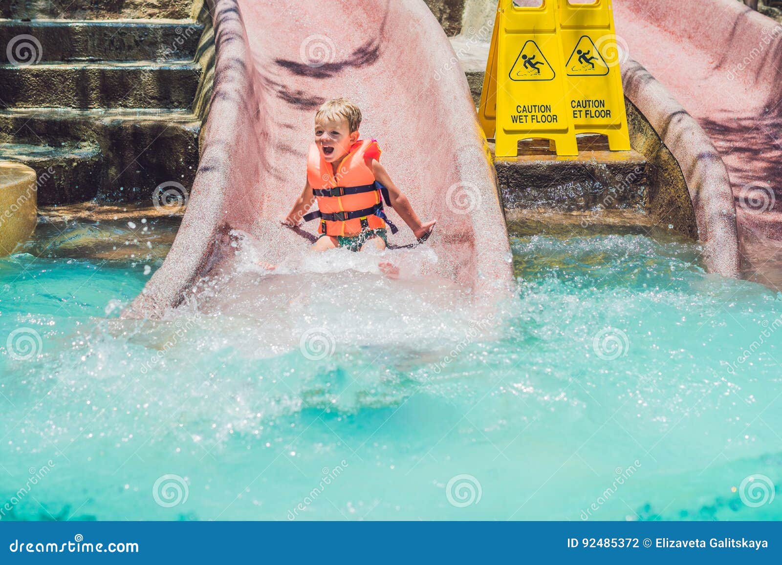 A Boy in a Life Jacket Slides Down from a Slide in a Water Park Stock