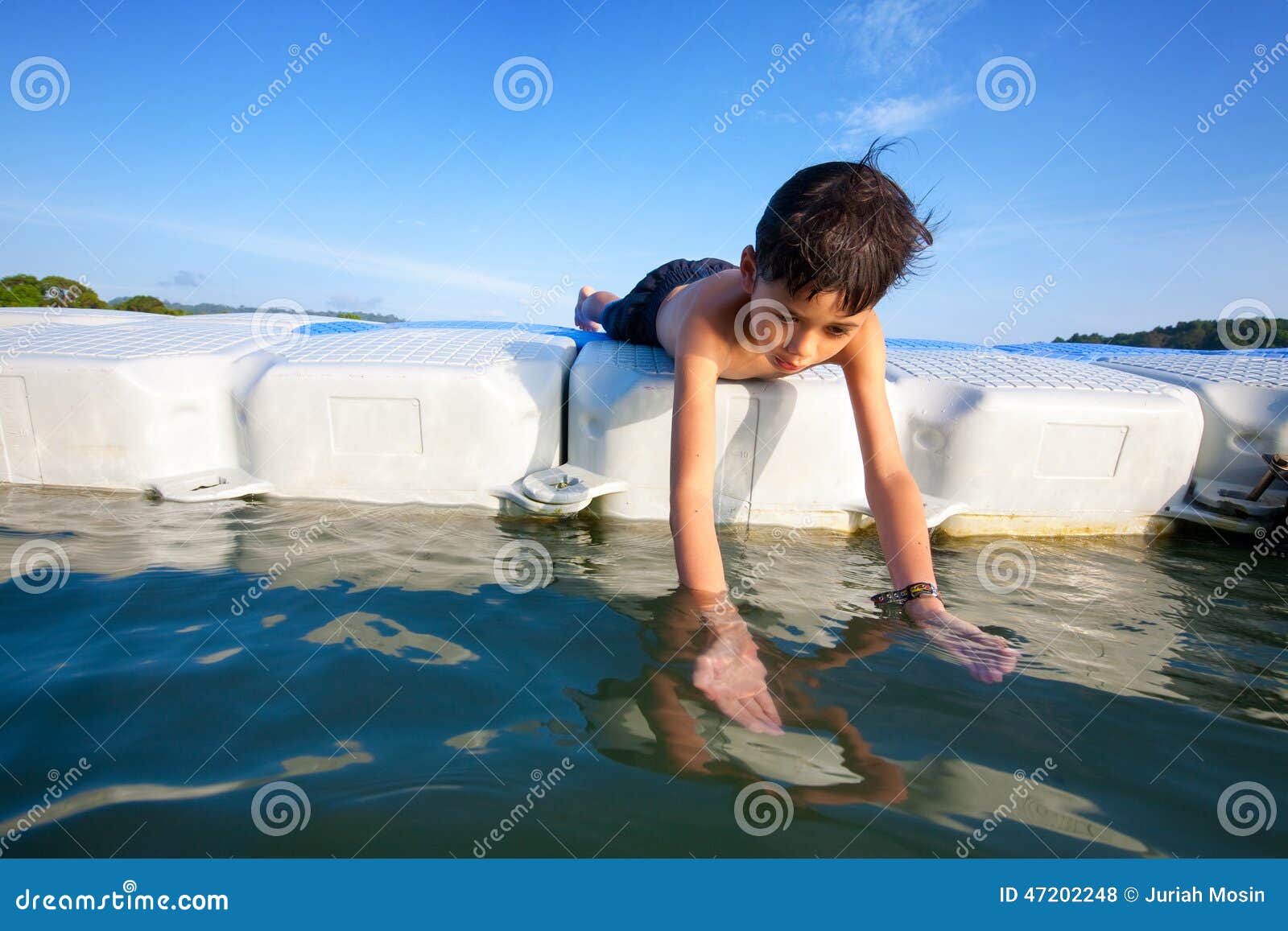Boy Lying on Floating Platform in Sea Trying To Catch Small Prawn Stock