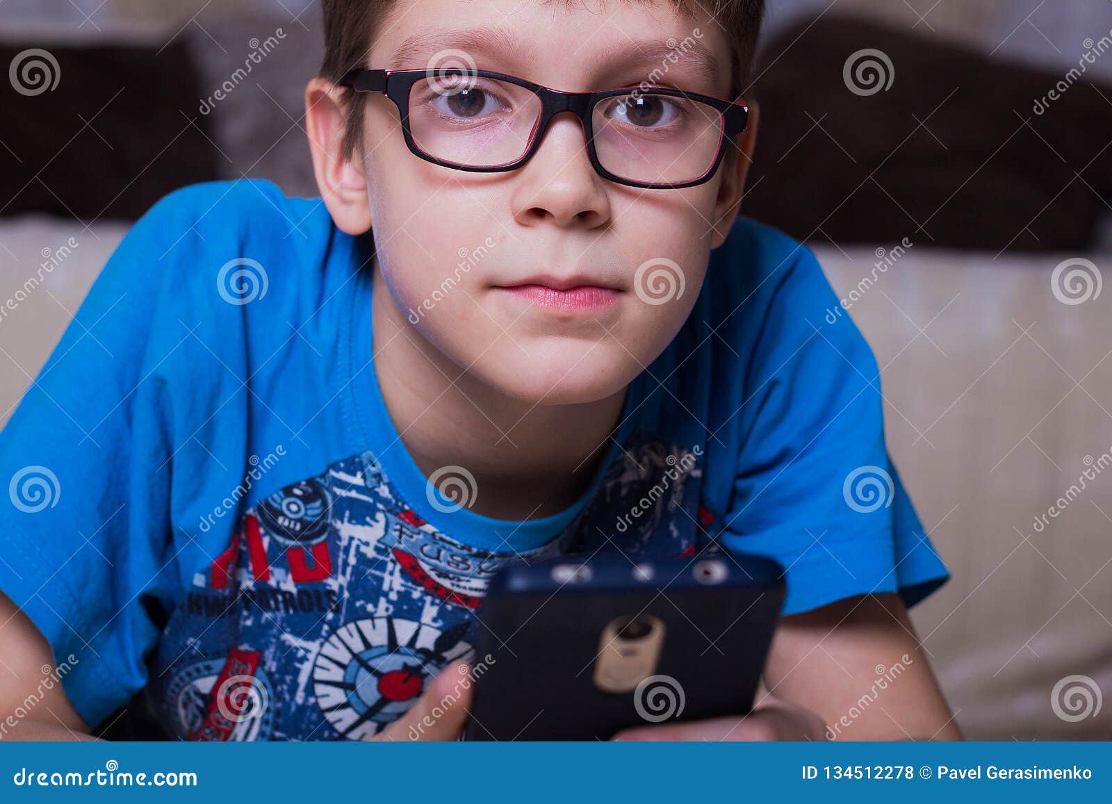 The Boy is Lying on the Floor, Holding a Smartphone and Looking at the ...