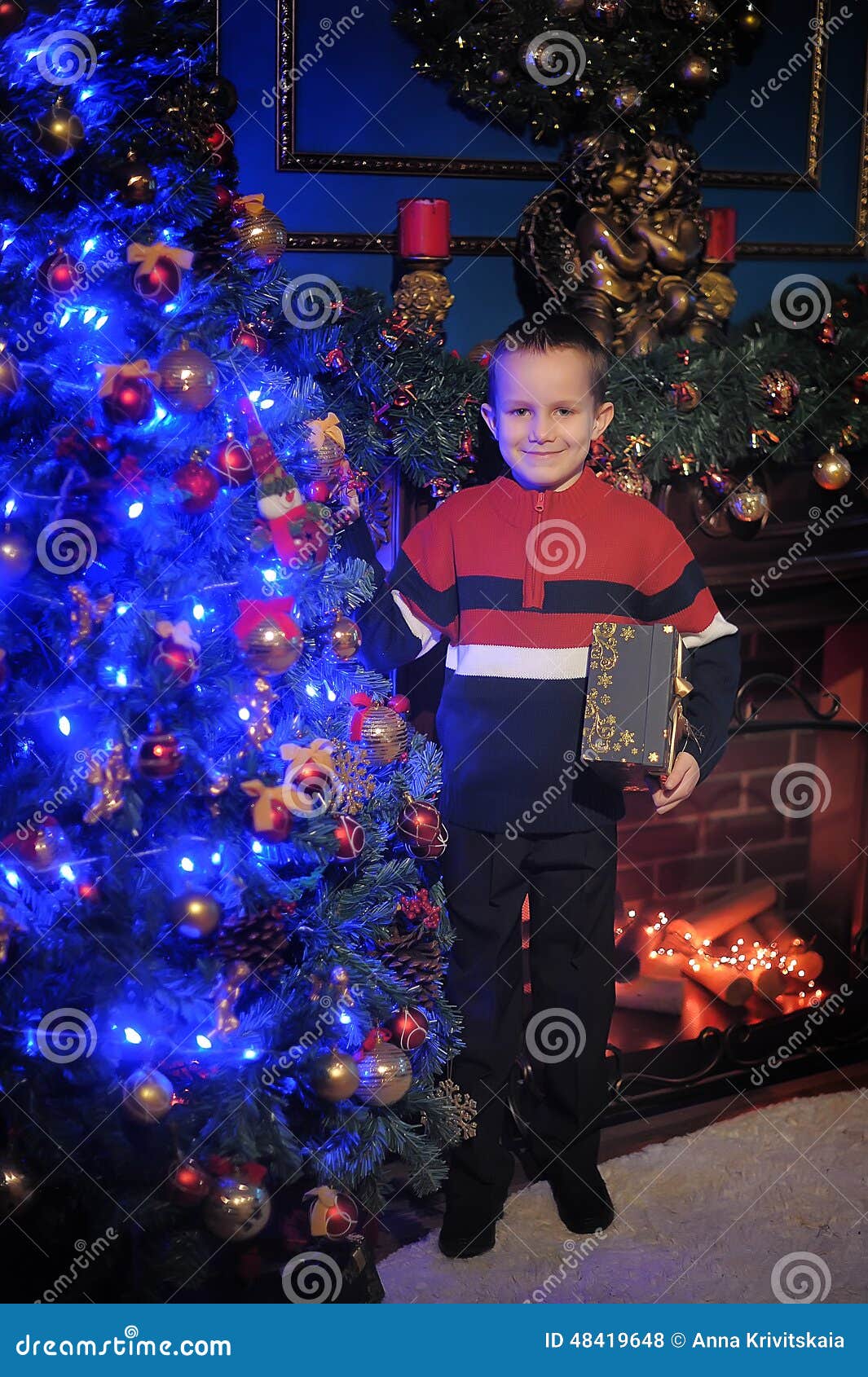 The boy next to a glowing blue Christmas tree and fireplace. Boy in a chair near the Christmas tree