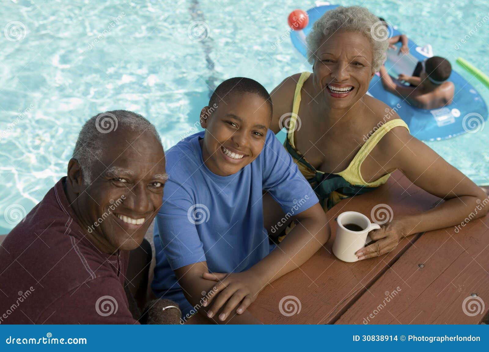 Boy (13-15) sitting with grandparents at picnic table by swimming pool 