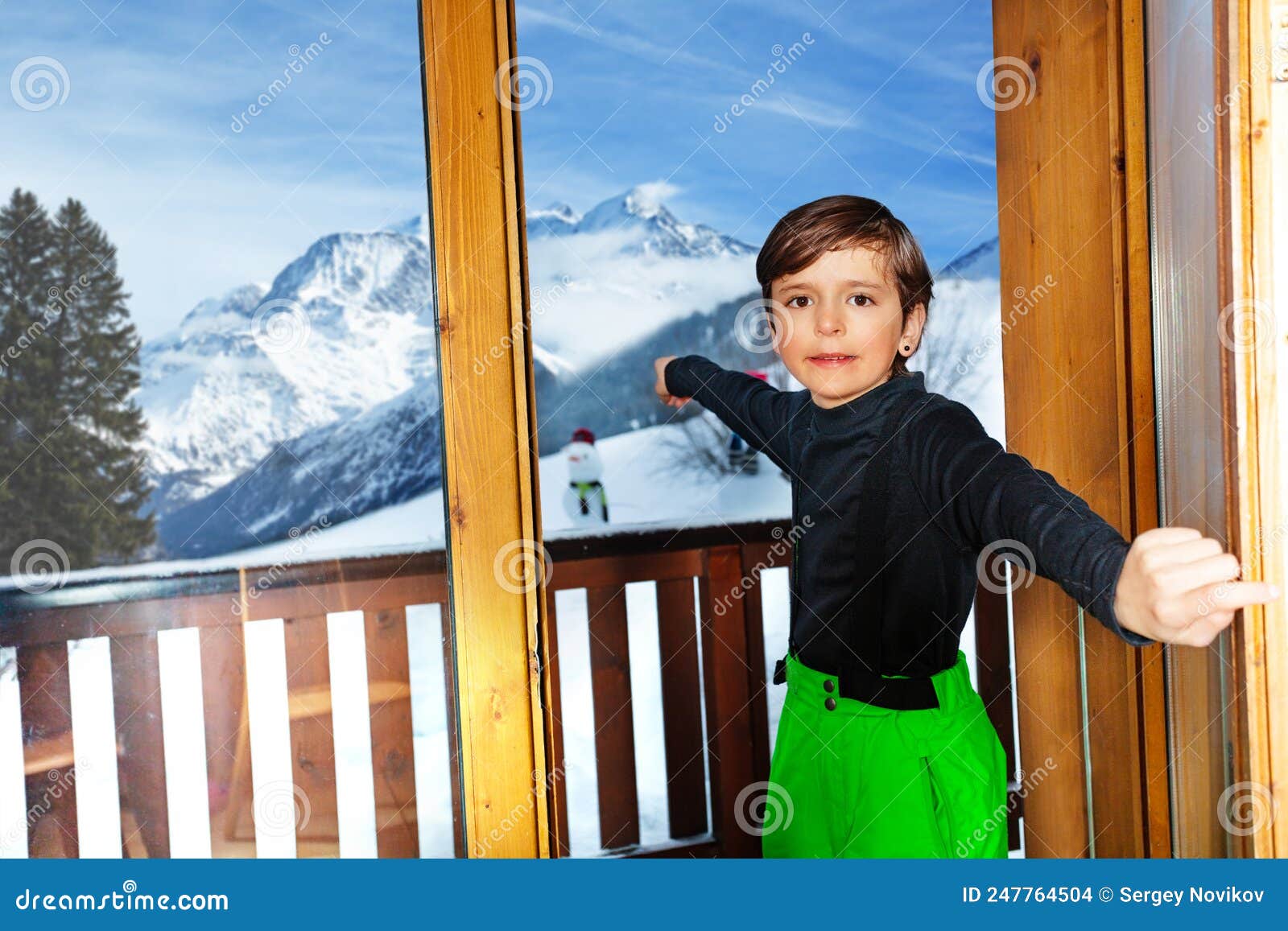 boy in ski outfit open the door to mountain peaks panorama