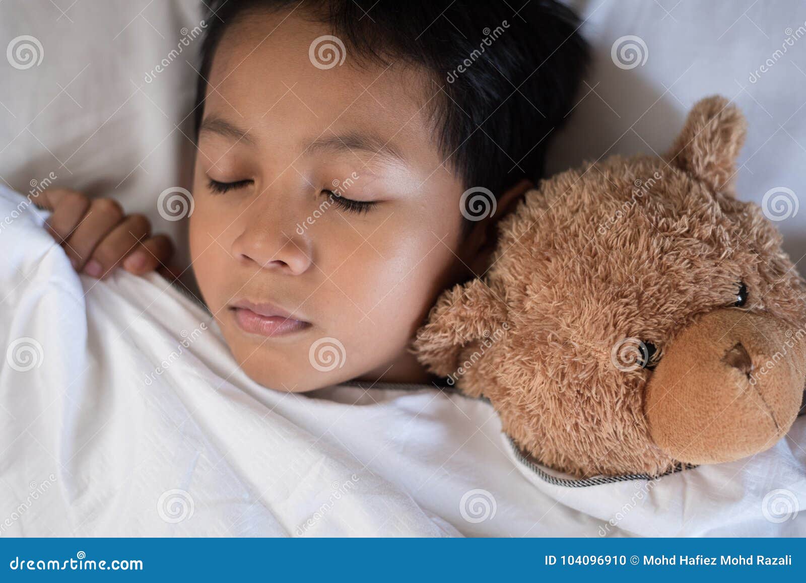 Boy Sleeping on Bed with Teddy Bear White Pillow and Sheets Stock Photo