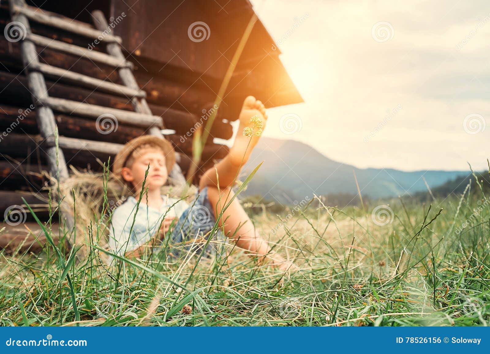 boy sleeps in grass under hayloft in summer afternoon