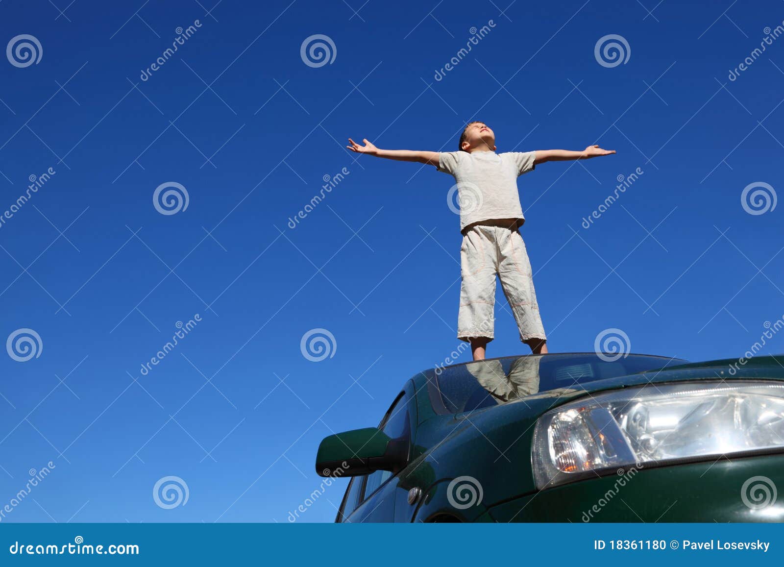 boy stands on head of car widely placing hands