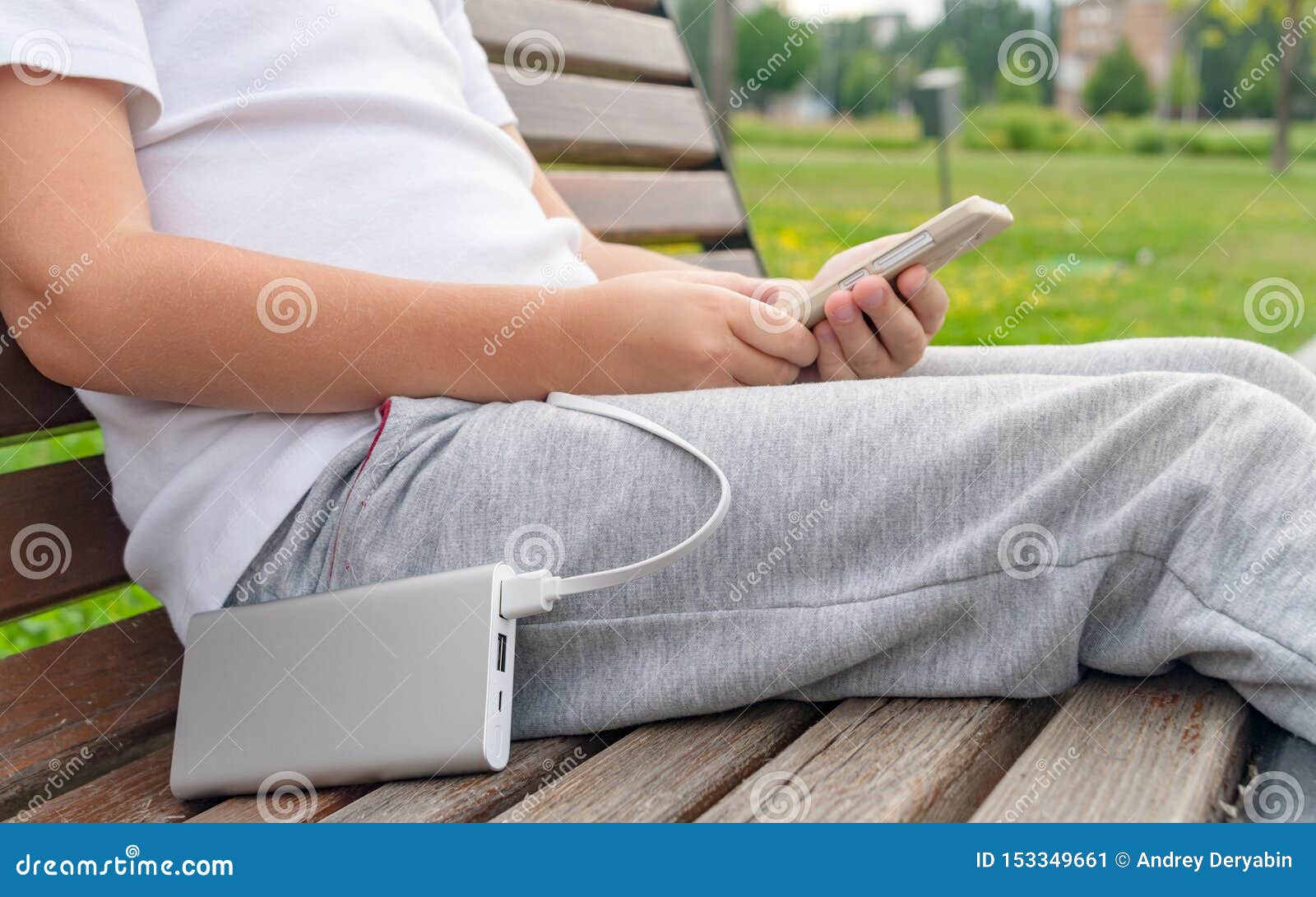 Boy using phone while charging from the power bank. Boy using phone on the bench while charging from the power bank