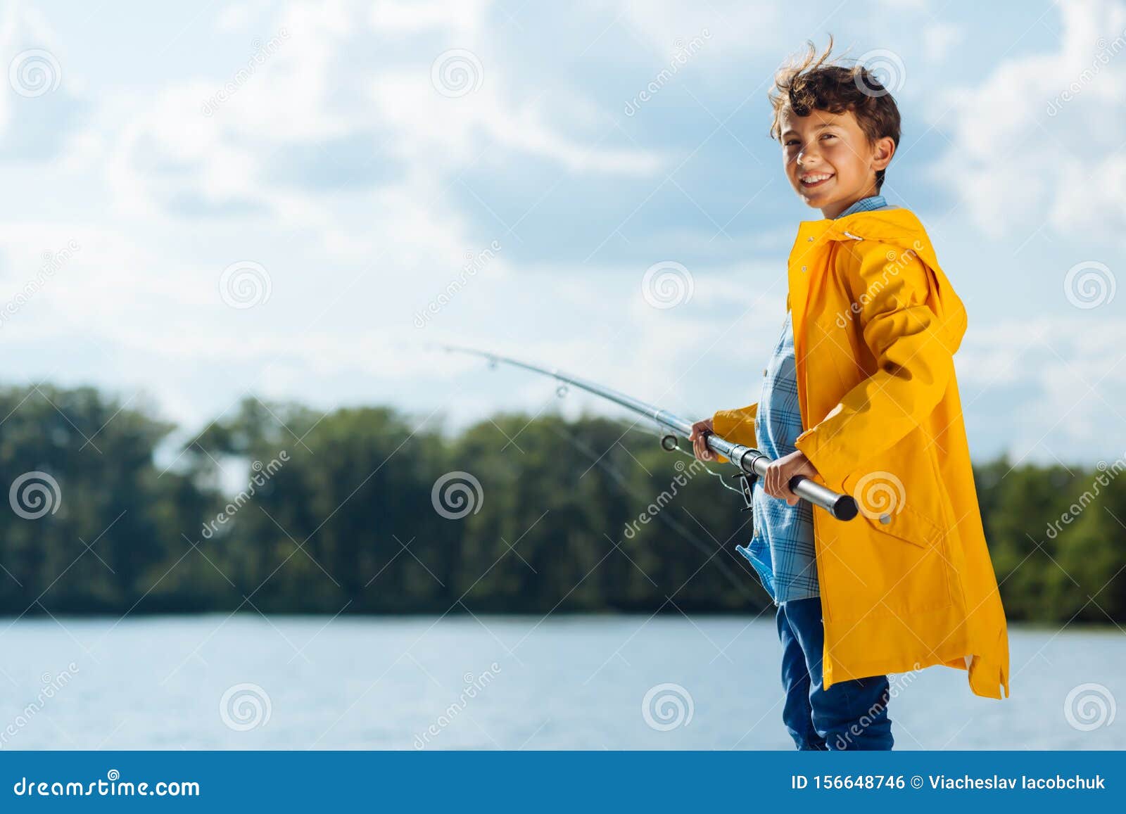 Boy Wearing Yellow Rain Coat Smiling while Fishing Stock Photo