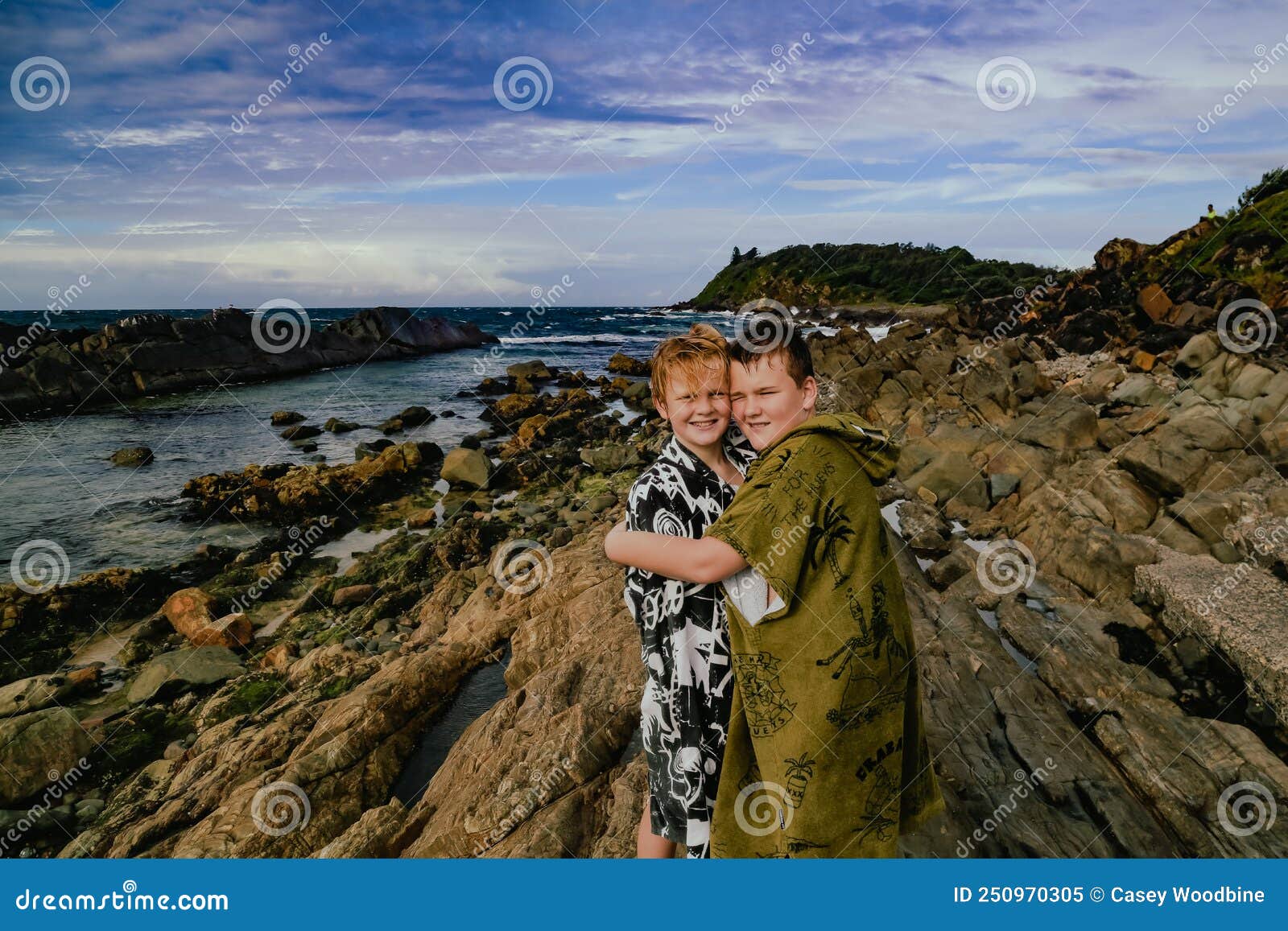 boys wearing hooded towels after swimming mucking around on rocks at the tanks tourist attraction at forster, nsw australia