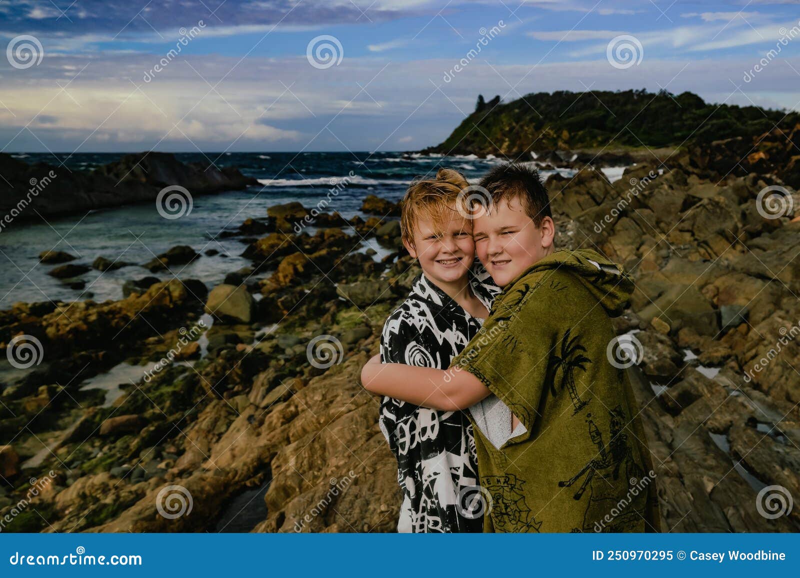 boys wearing hooded towels after swimming mucking around on rocks at the tanks tourist attraction at forster, nsw australia