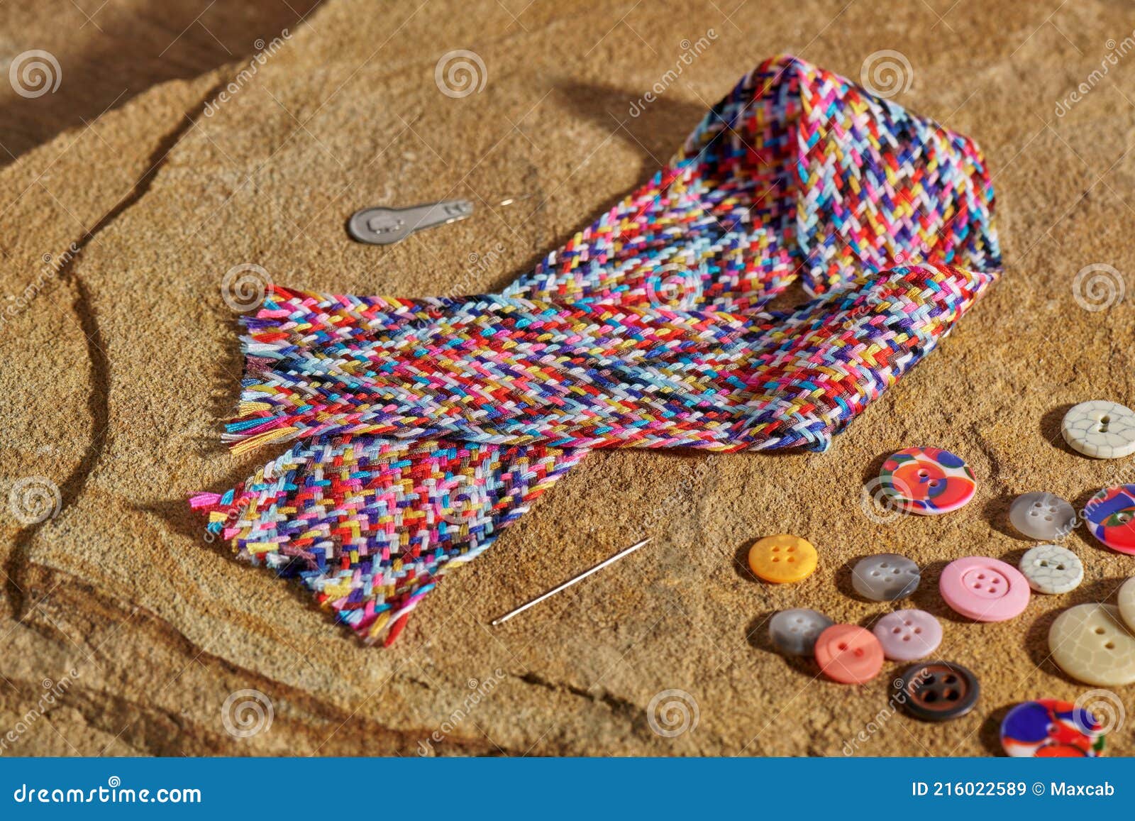 a braid of multi colored sewing threads, needle, needle threader, buttons lying on a stone