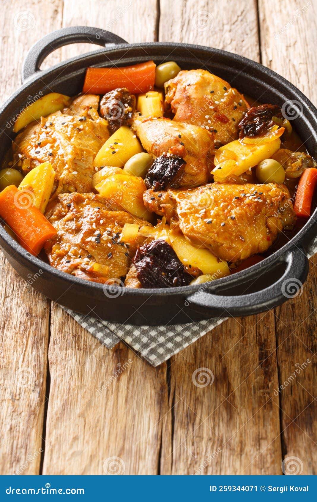 braised chicken meat with spicy sauce, prunes, carrots, potatoes, olives and onions close-up in a frying pan. vertical