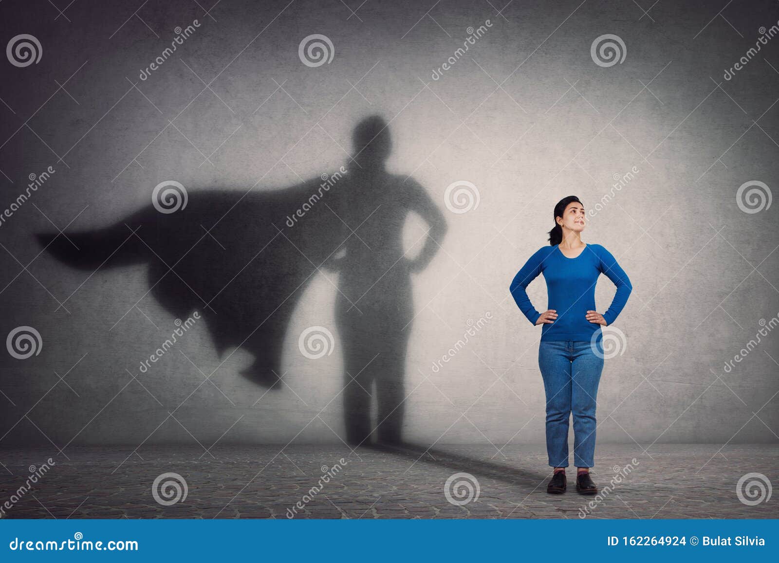 brave woman keeps arms on hips, smiling confident, casting a superhero with cape shadow on the wall. ambition and business success