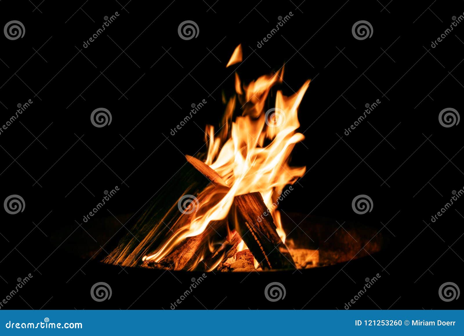 brazier or fire bowl with burning wood logs in front of black ba