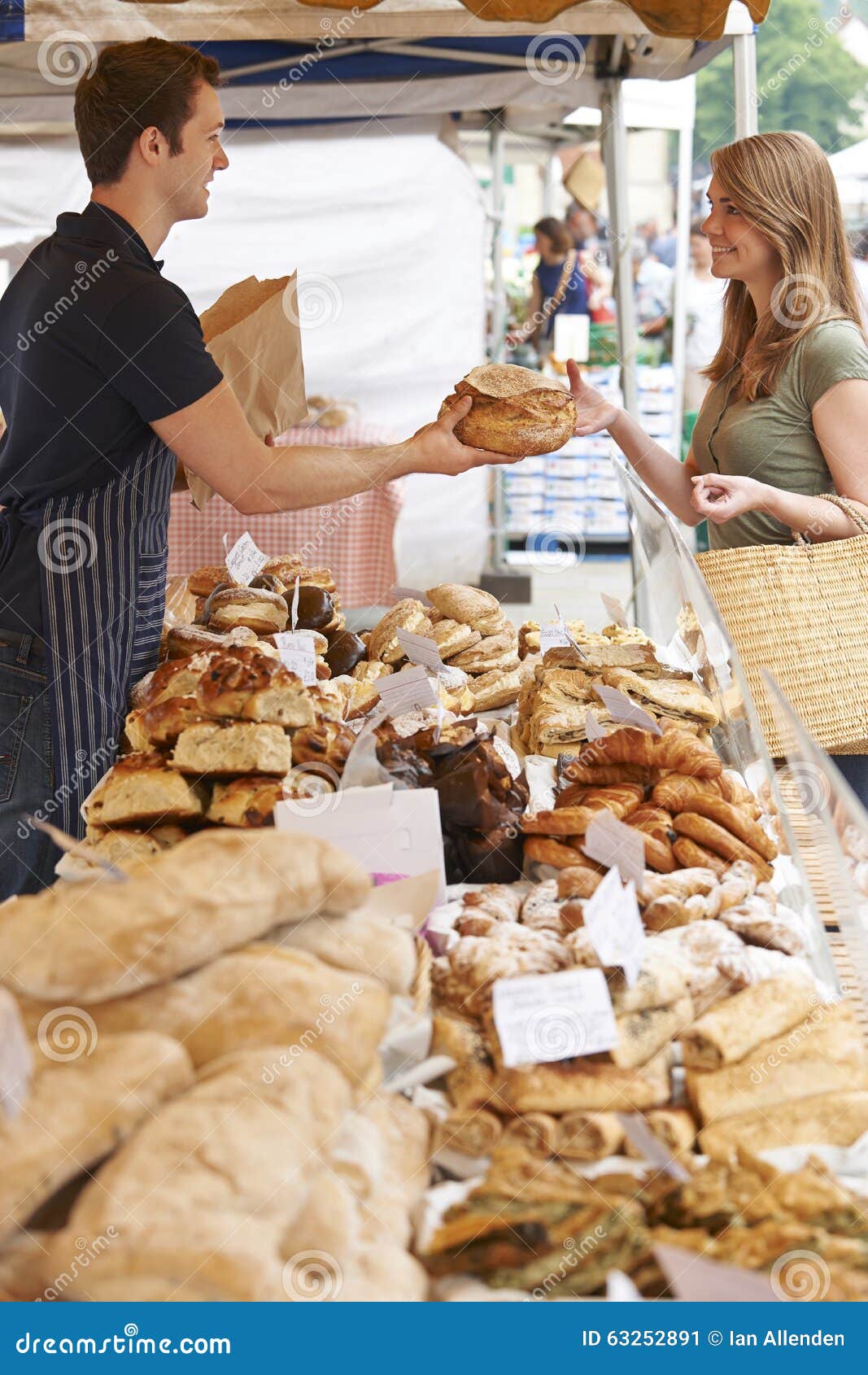 Bread Stall Owner at Market Serving Customer with Loaf Stock Image