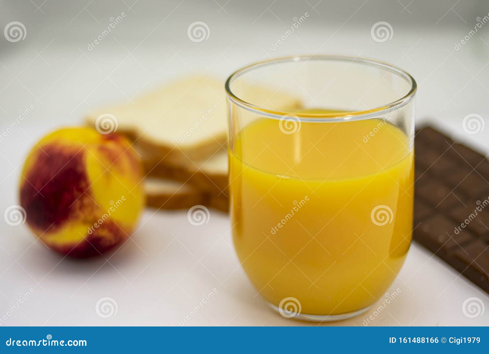 breakfast consisting of natural orange juice, ripe peach, white bread and milk chocolate