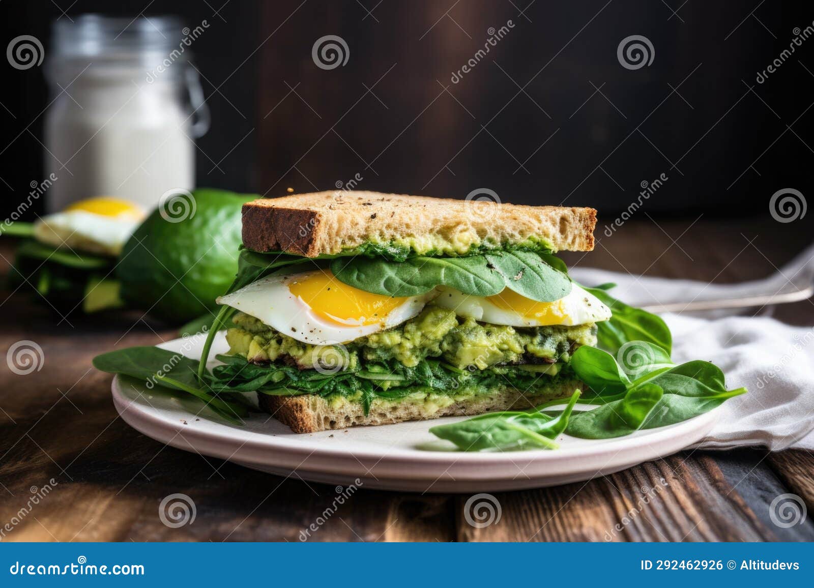 A Breakfast Sandwich with Avocado, Spinach, and Egg on a Rustic Table