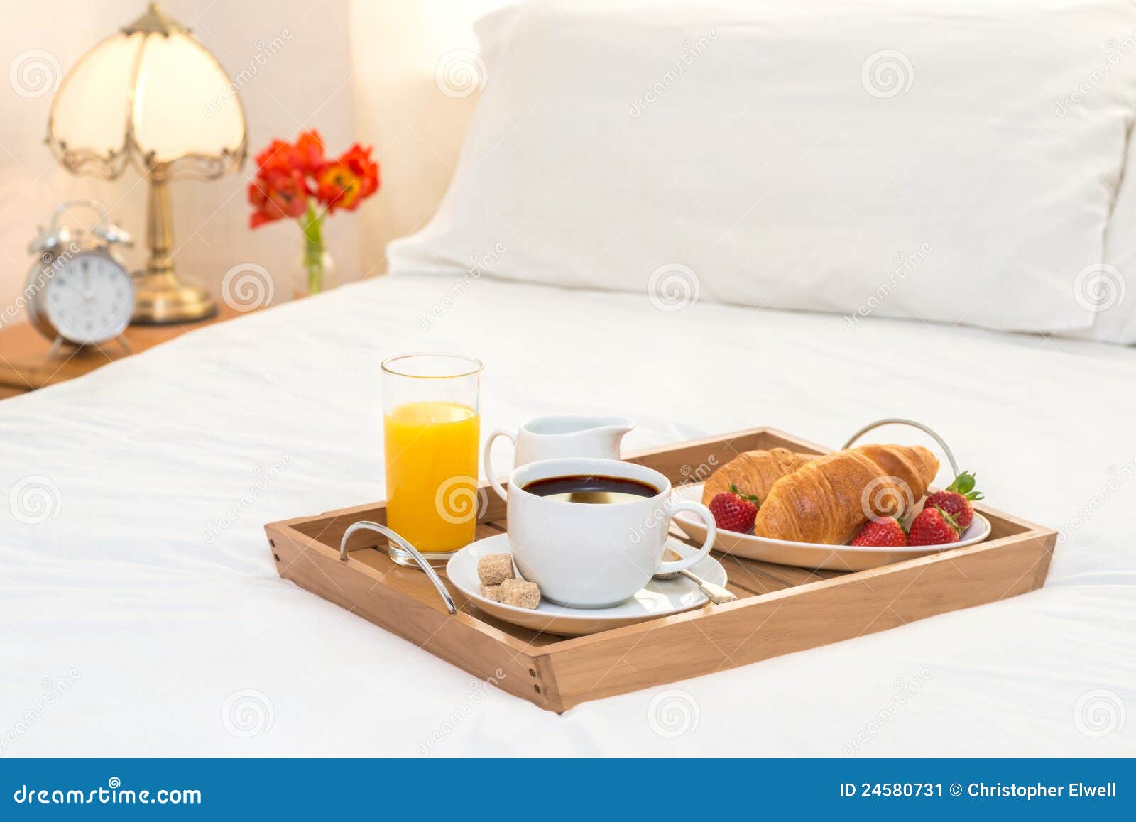 Breakfast served in bed on wooden tray with coffee and croissants.