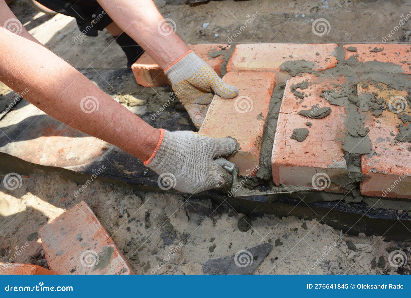Bricklayer Hands Laying the First Course of Bricks on House Foundation