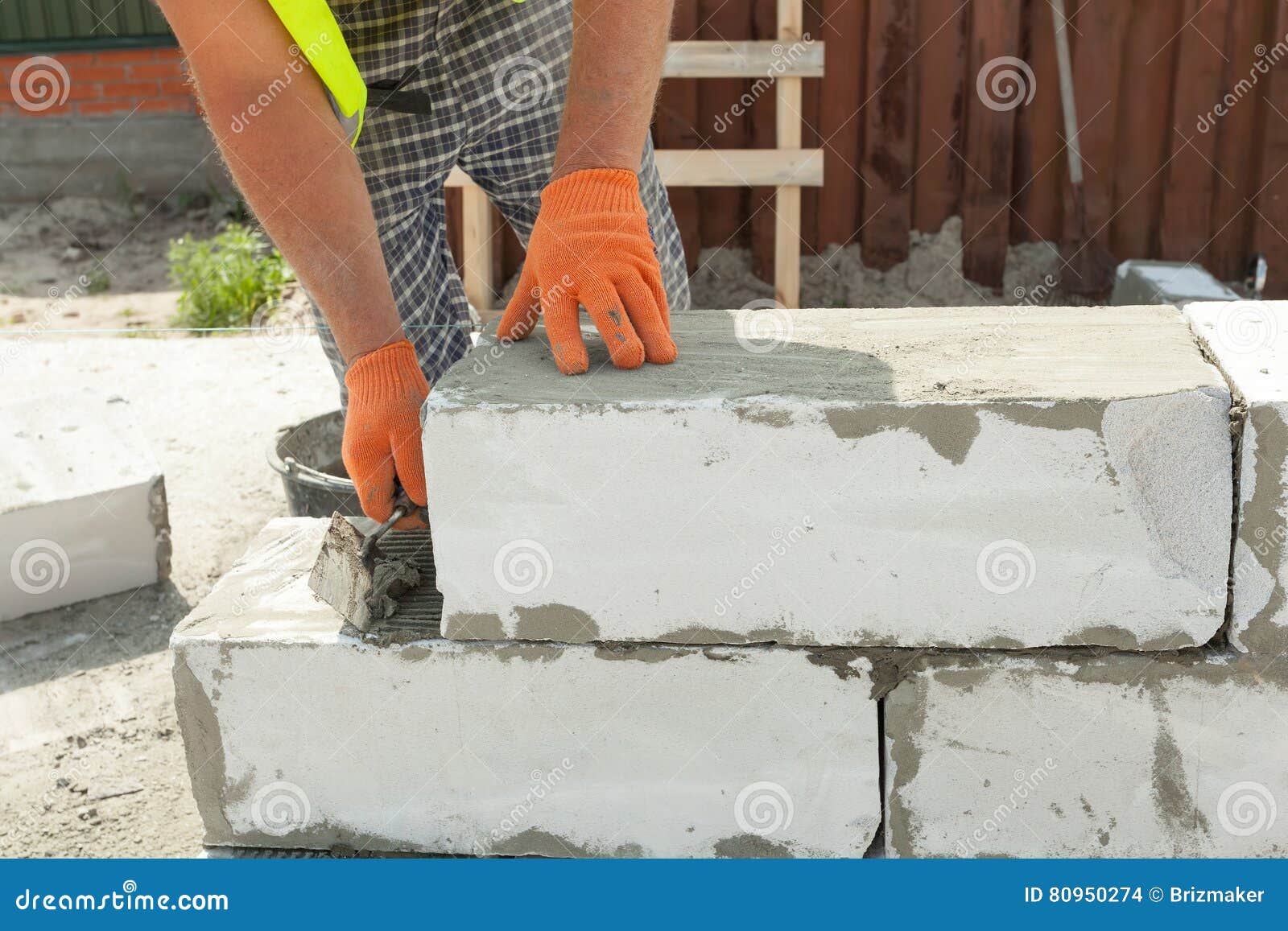 Bricklayer Man Worker in Orange Gloves Installing Block with Trowel