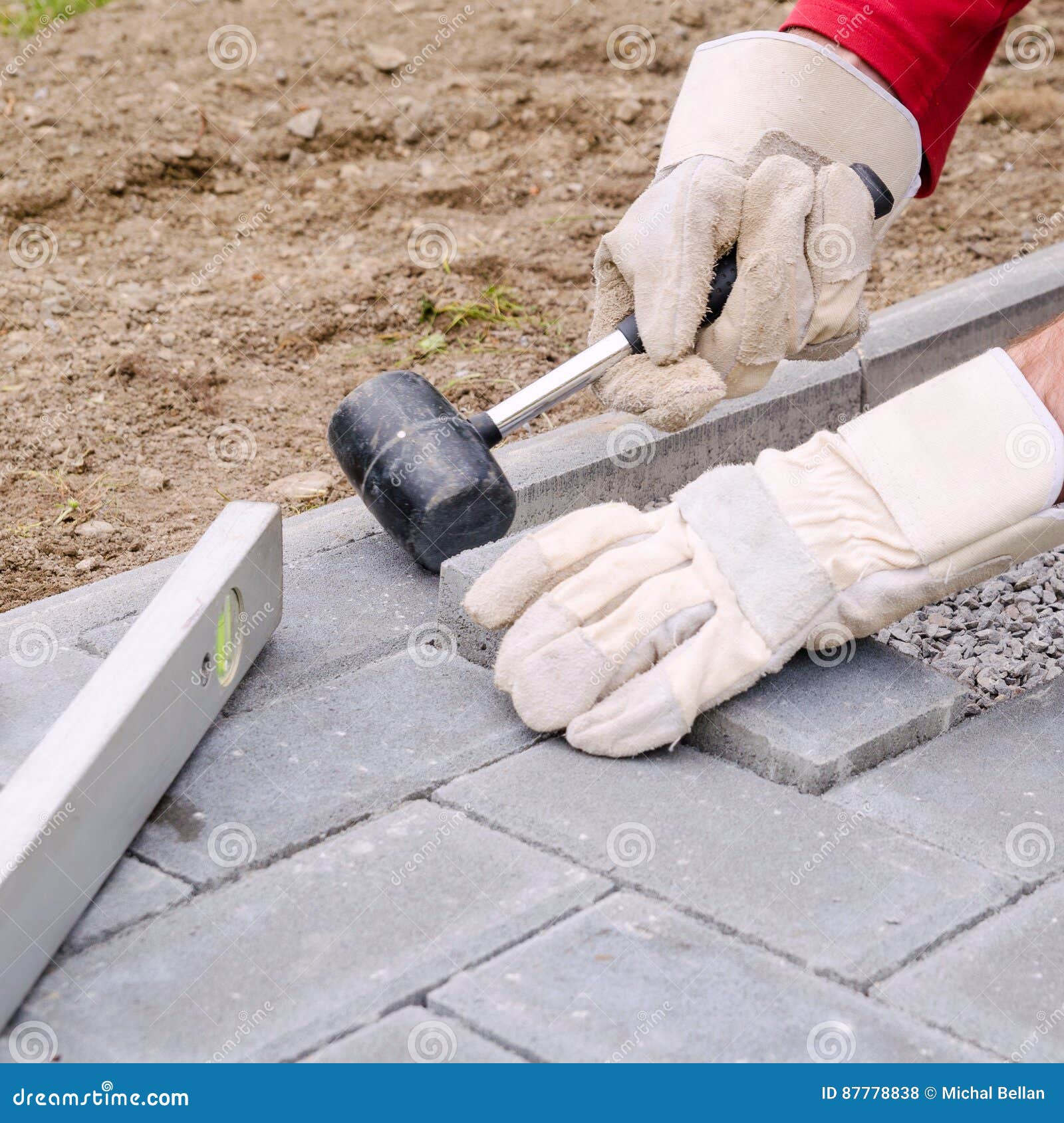 bricklayer places concrete paving stone blocks for building up a pave patio, using hammer and spirit level. handyman diy concept