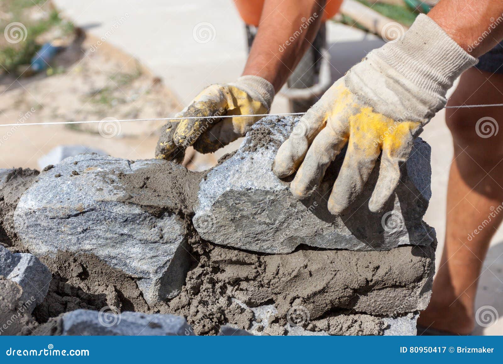 Bricklayer Worker in Protection Yellow Gloves Installing Stones. Stock