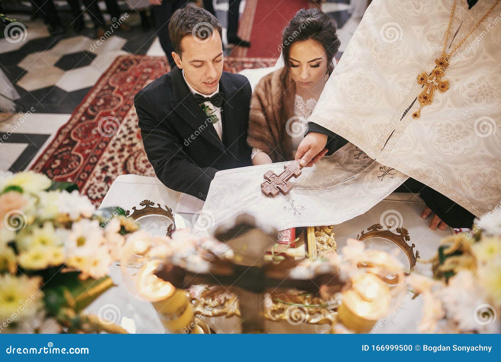 bride and groom pronouncing vows, holding hands on bible on altar and priest holding golden cross on hands during holy matrimony