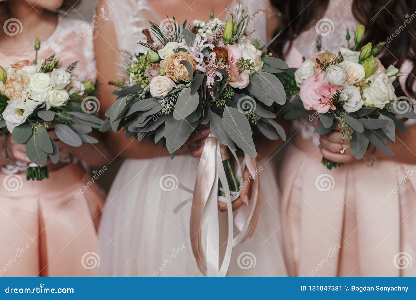 bridesmaids and bride holding modern wedding bouquets of pink roses and green eucalyptus with pink ribbons. stylish contemporary