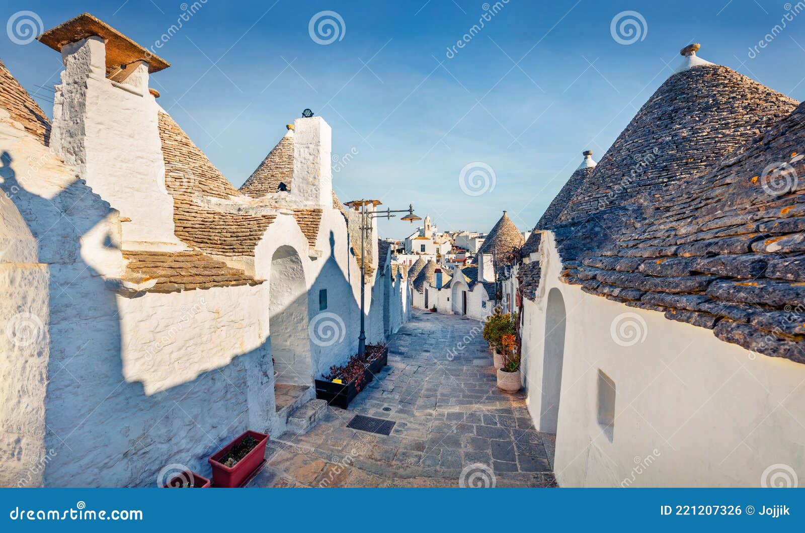 bright morning view of empty strret with trullo trulli -  traditional apulian dry stone hut with a conical roof. amazing summer