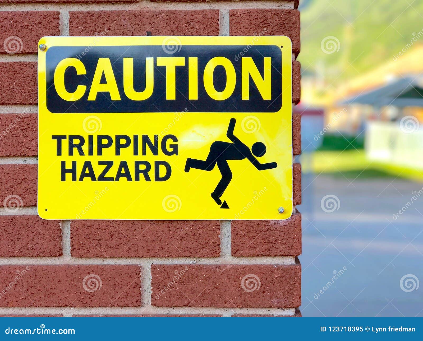 humorous yellow caution sign on red brick wall with stick man illustrating tripping hazard