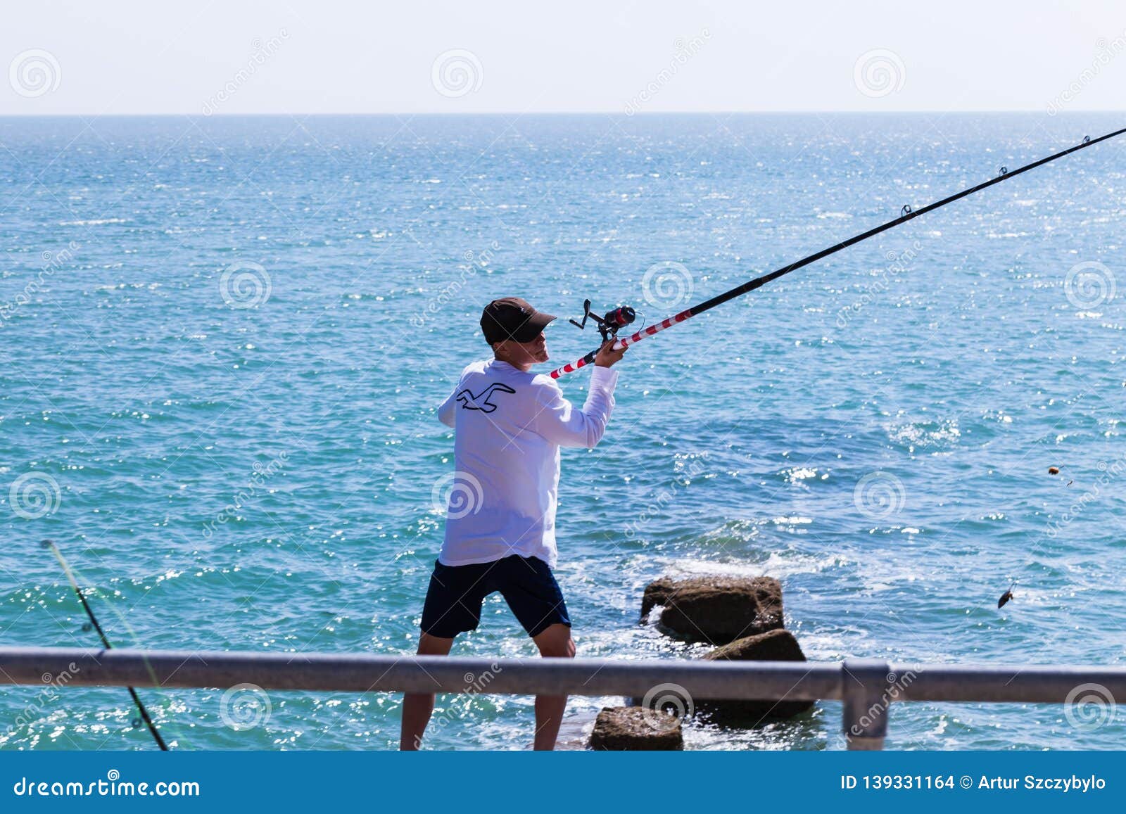 https://thumbs.dreamstime.com/z/brighton-uk-june-man-cap-standing-shore-holding-sideways-long-fishing-rod-reel-crystal-blue-wavy-water-sunny-day-sport-139331164.jpg