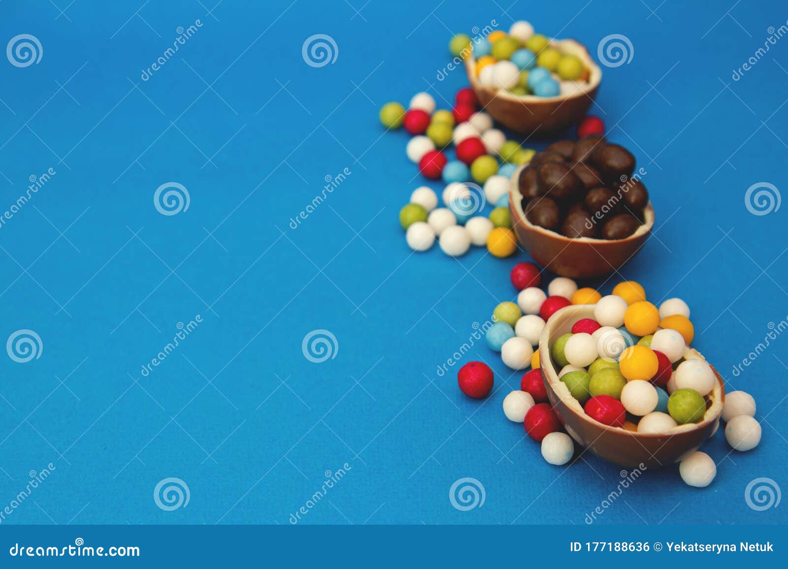 broken chocolate easter eggs and strew colored sweets on blue background