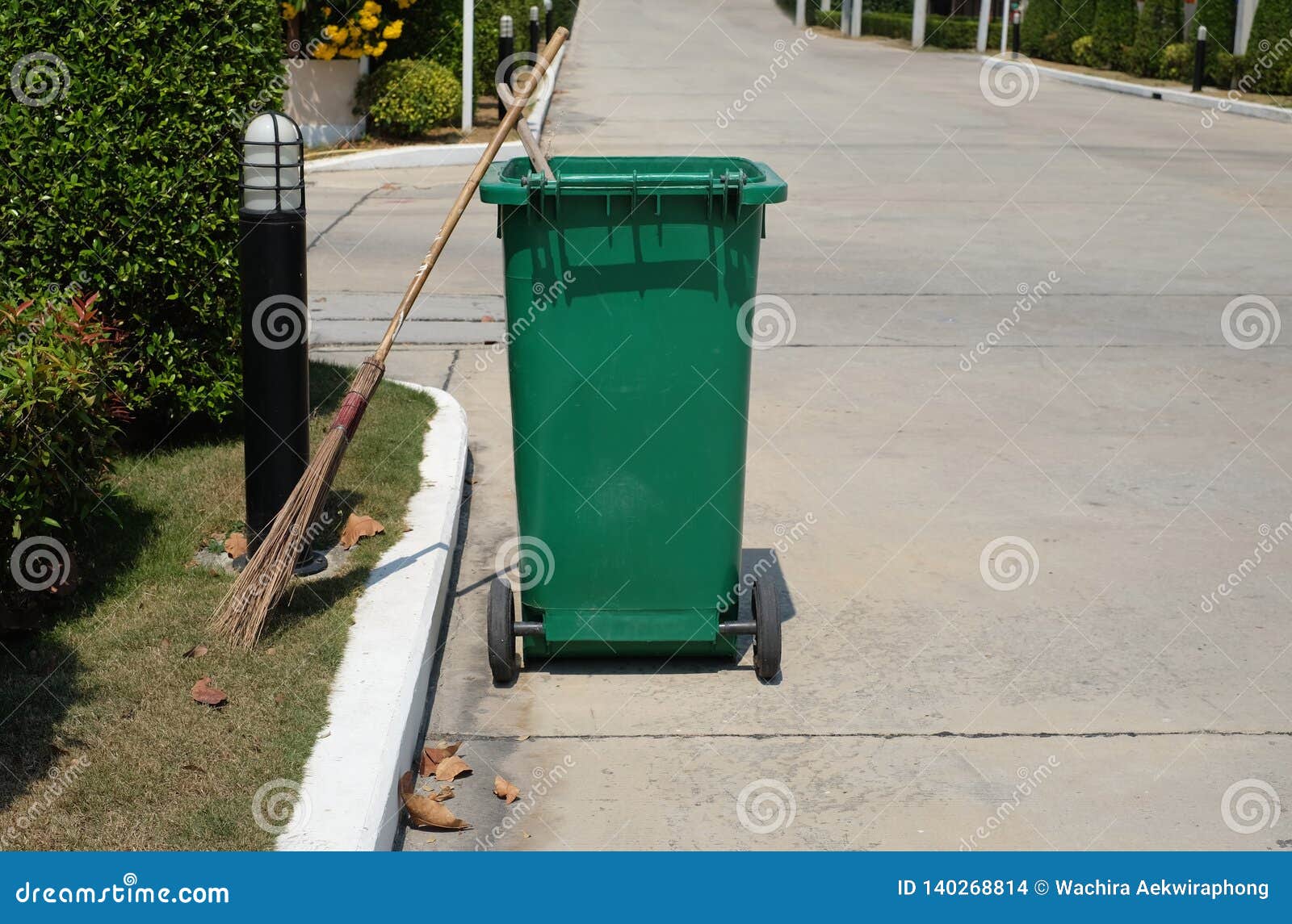 Broom and Green Bin Placed Next To the Roadside Path Stock Photo
