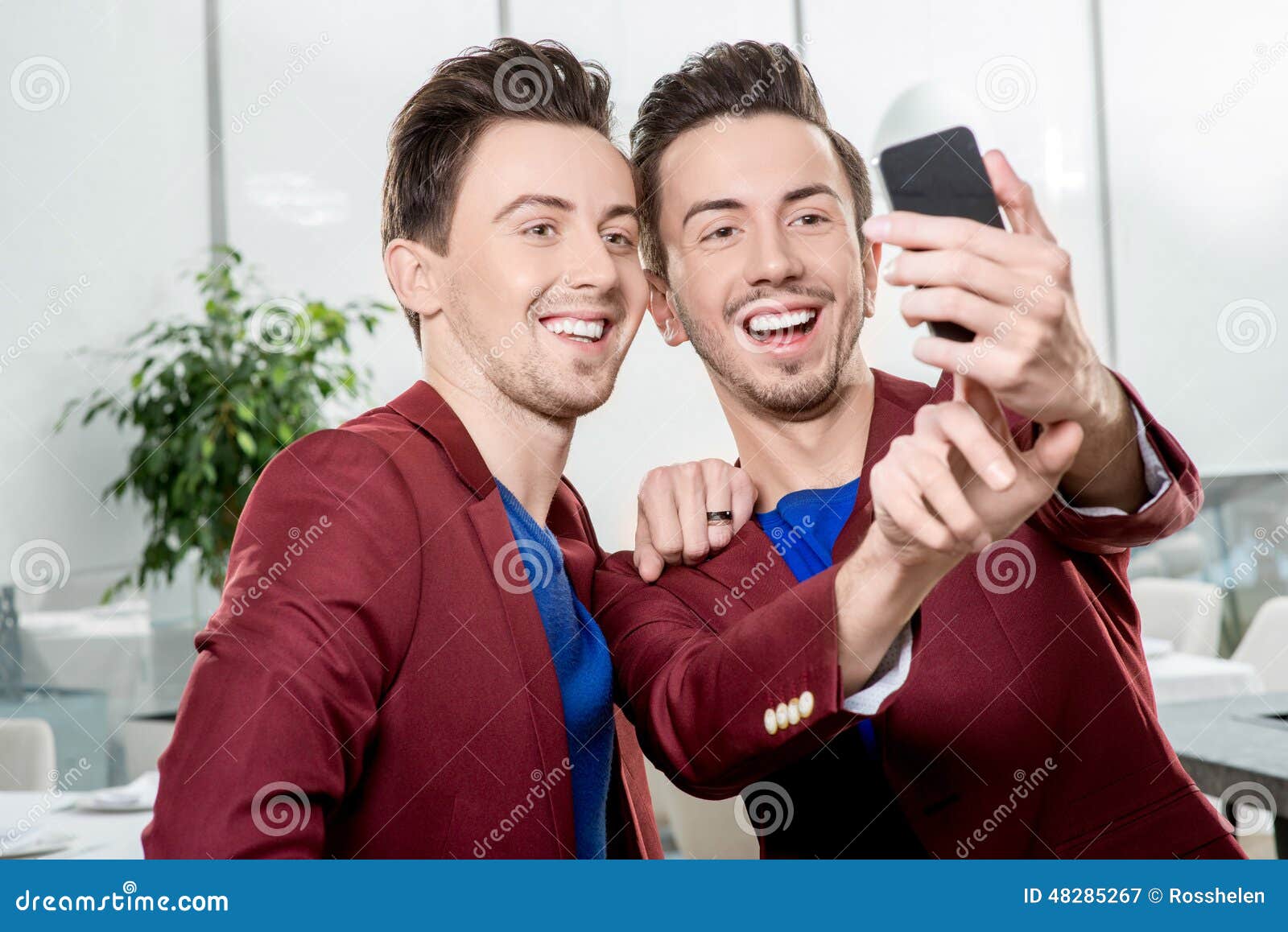 Brothers twins taking selfie photo. Friendly brothers twins having fun taking selfie photo with smart phone in the white home or restaurant interior