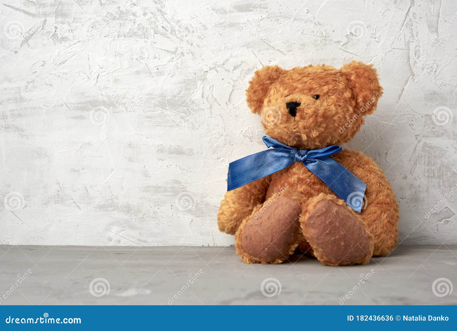 Brown Teddy Bear with a Blue Bow Sits on a White Background Stock Photo