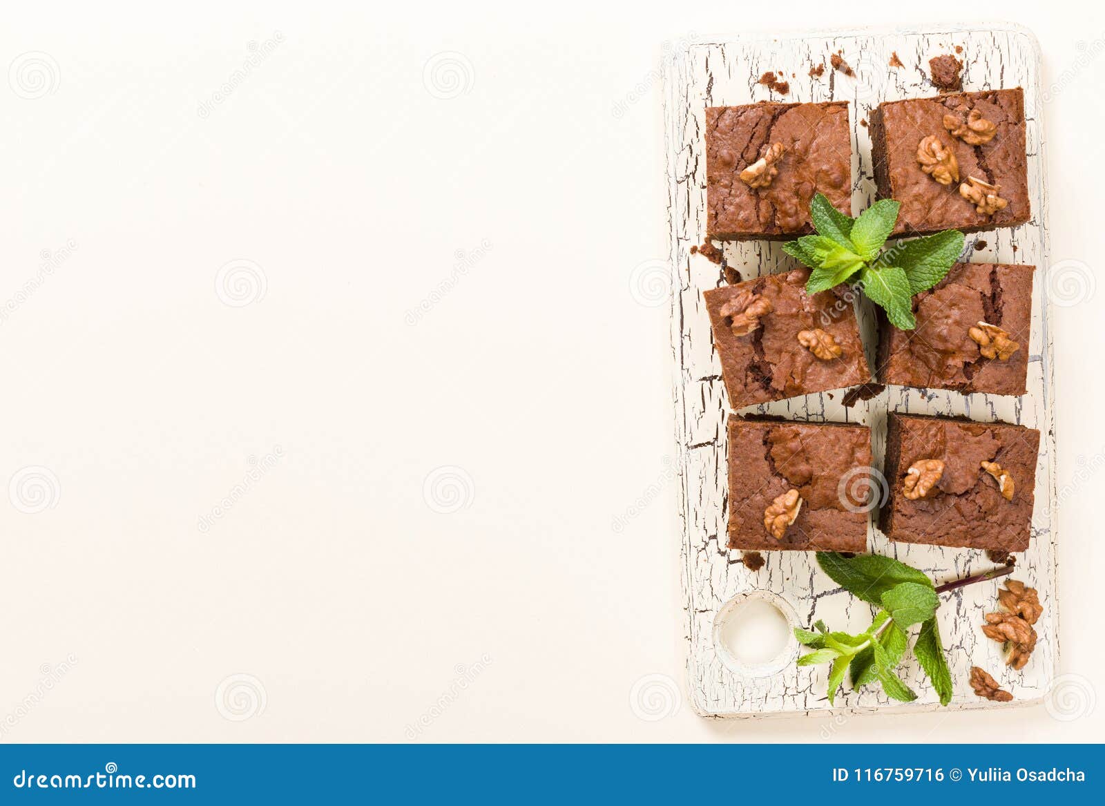 brownie sweet chocolate dessert with walnuts and meant leaves on retro board with copy space on pastel beige background.