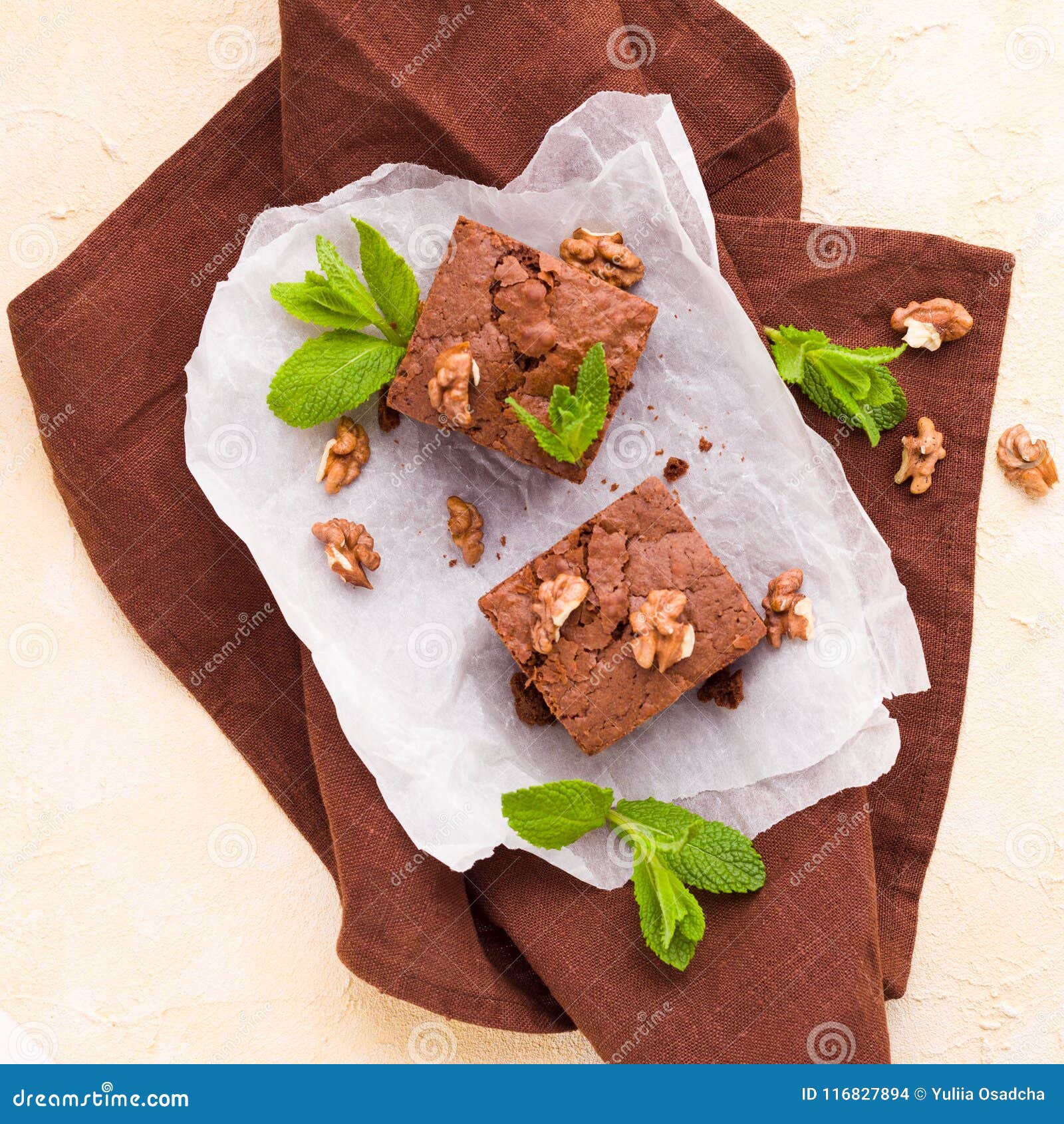 brownie sweet chocolate dessert with walnuts and meant leaves on white paper with copy space on pastel beige background.