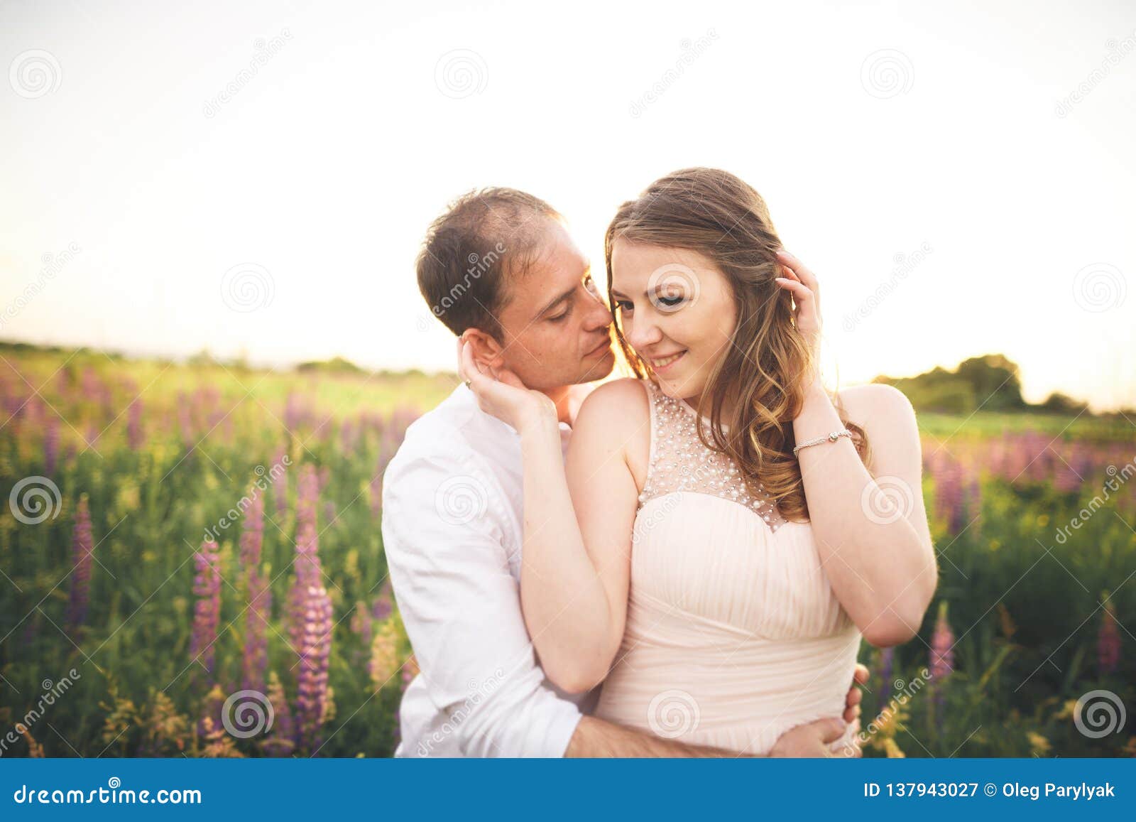 Brud och brudgum som rissing på solnedgången på ett härligt fält med blommor, romantiskt gift par