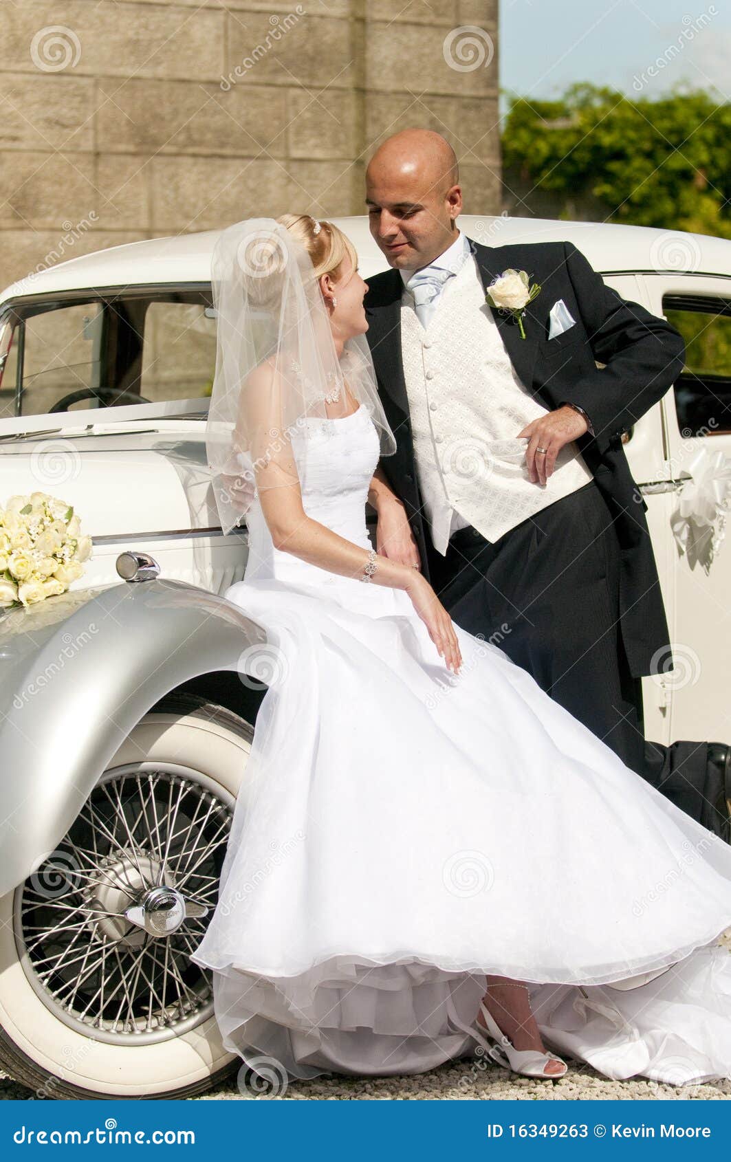 Overweldigen die bruid en bruidegom naast een uitstekende huwelijksauto kijkt