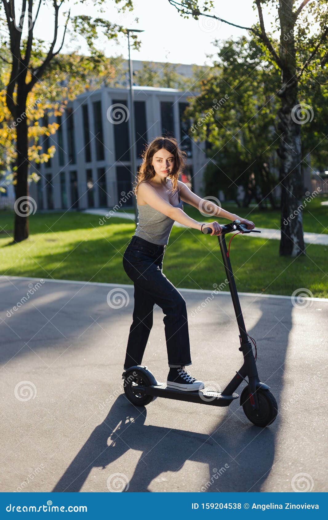 Brunette Girl Riding an Eco-friendly Electric Kick Scooter in a Park in ...