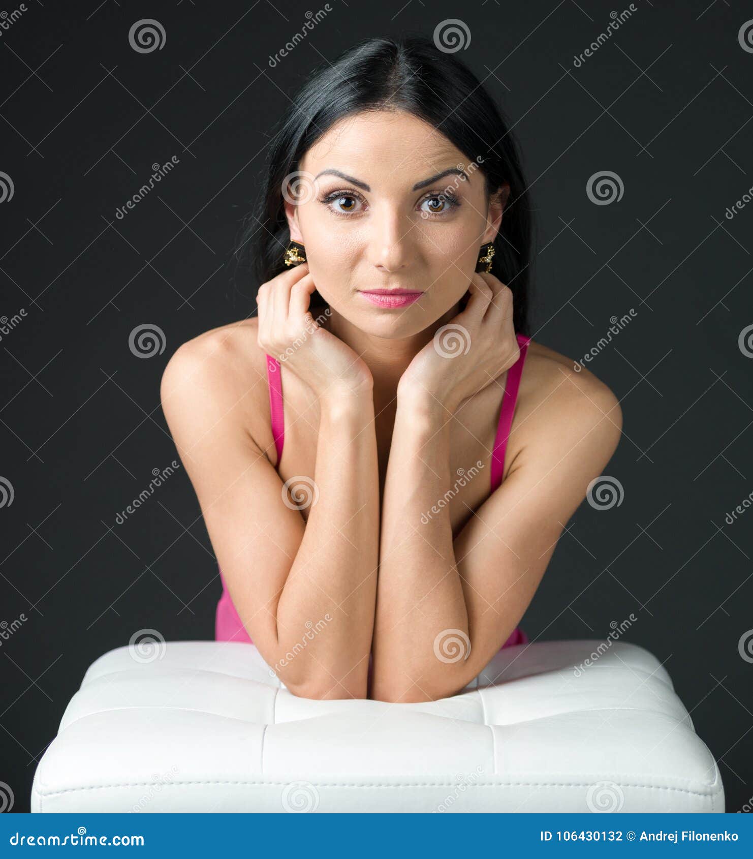 brunette with green eyes and in a pink nightie posing, leaning elbows on a white ottoman
