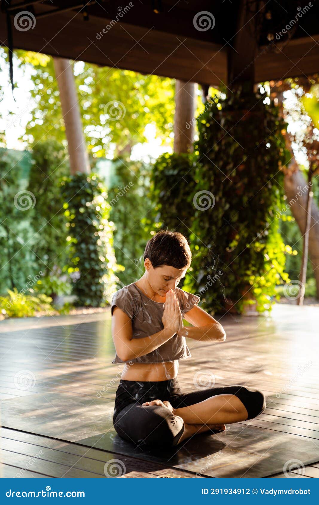 Brunette Woman Doing Yoga While Sitting On Wooden Floor Outdoors Stock Brunette Woman Doing Yoga While Sitting On Wooden Floor Outdoors Stock