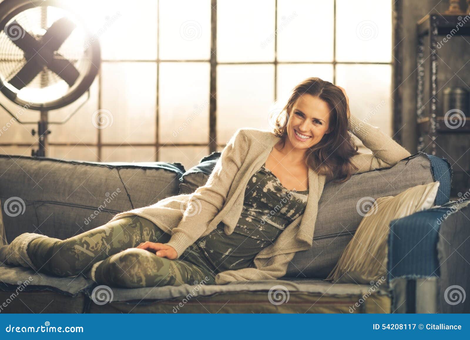 A Brunette Woman is Smiling, Relaxing on a Sofa Stock Image