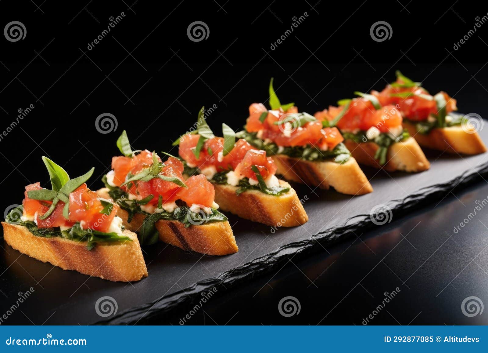 bruschetta set in a diagonal line on a black slate surface, each topped with a leaf of fresh basil