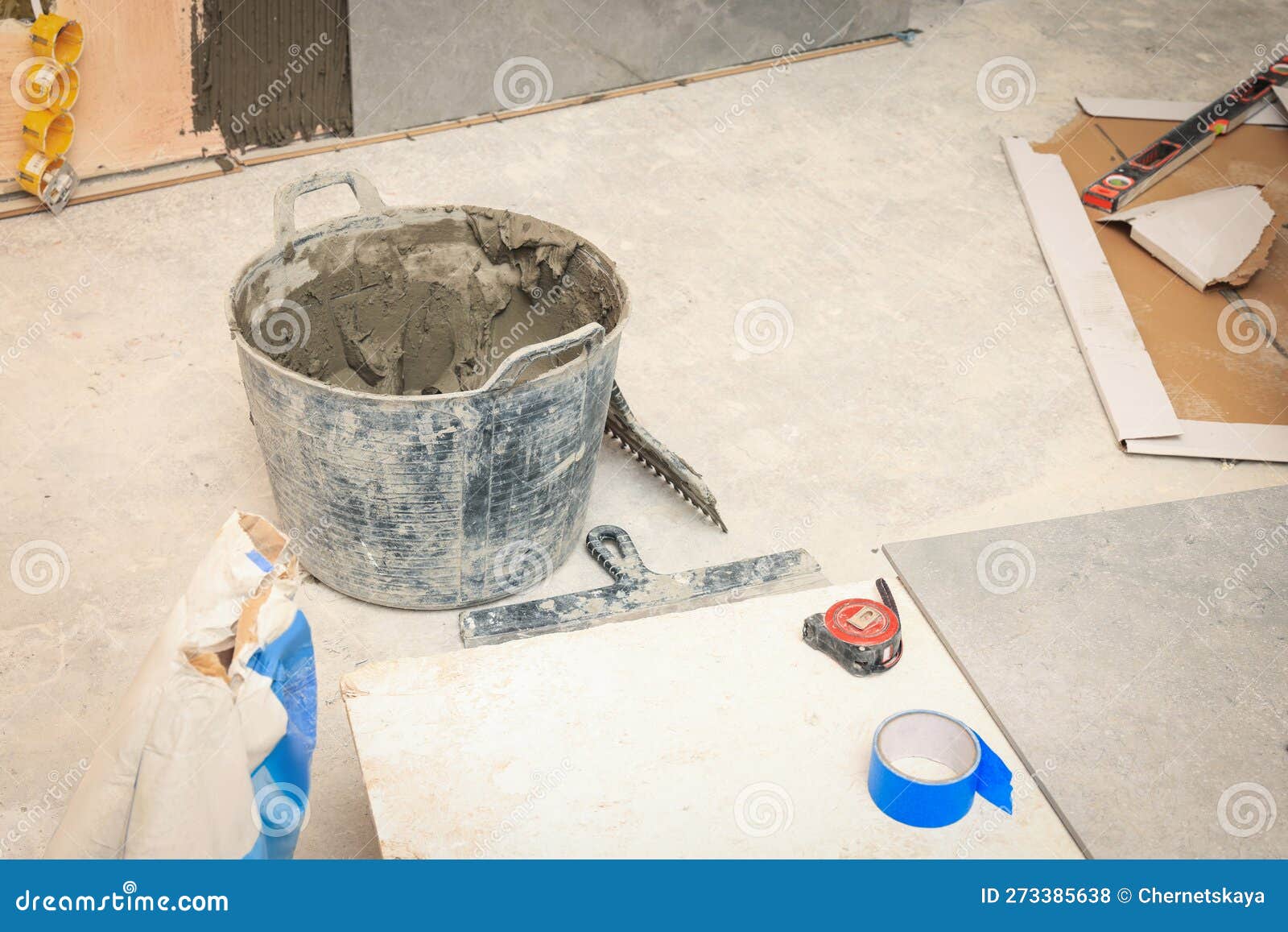 Bucket of Adhesive Mix and Different Tools on Floor Indoors. Tile