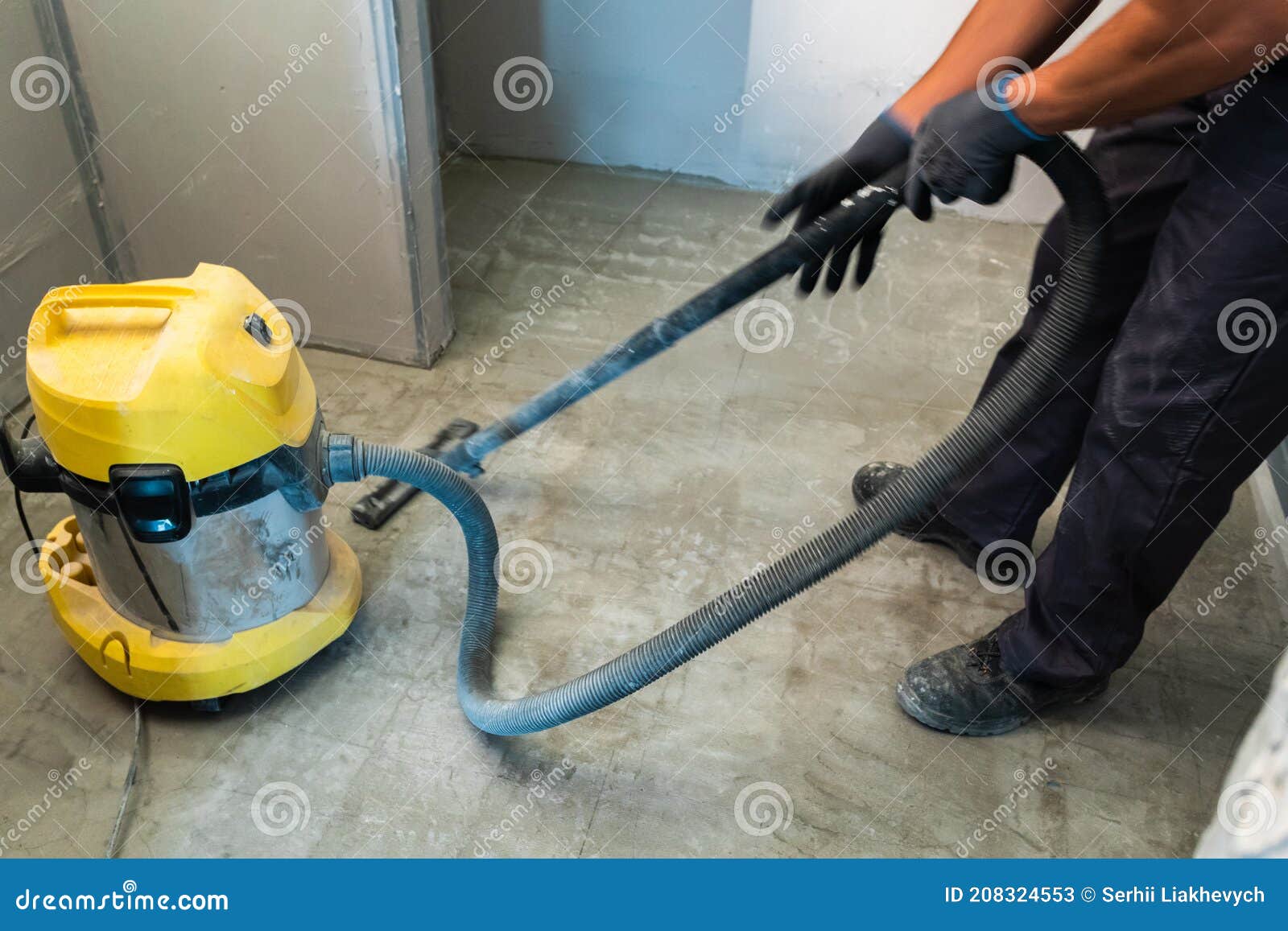 The Builder Cleans the Floor from Dust with a Construction Vacuum