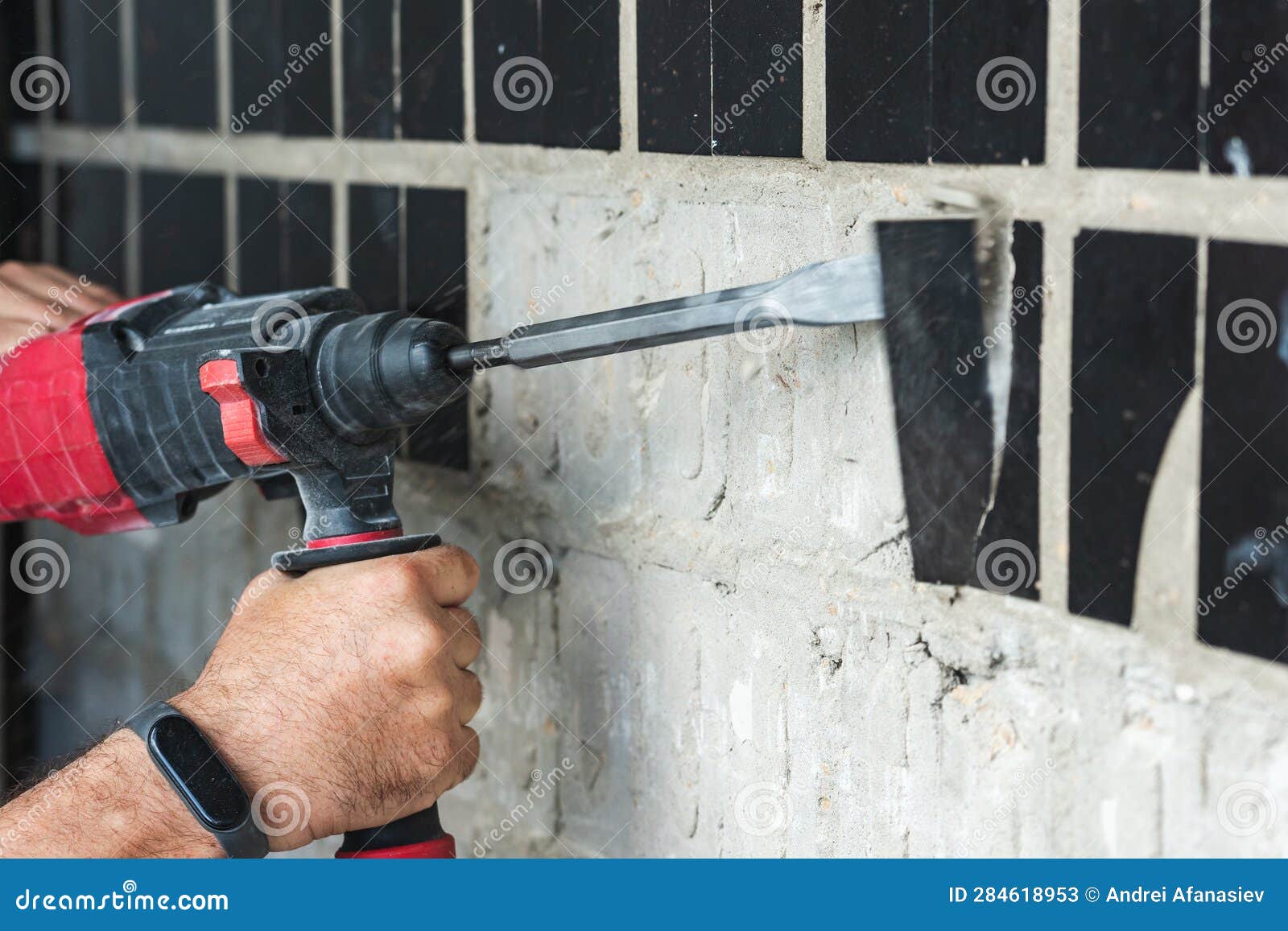 Builder with a Puncher Dismantles Old Tiles from a Concrete Wall Stock