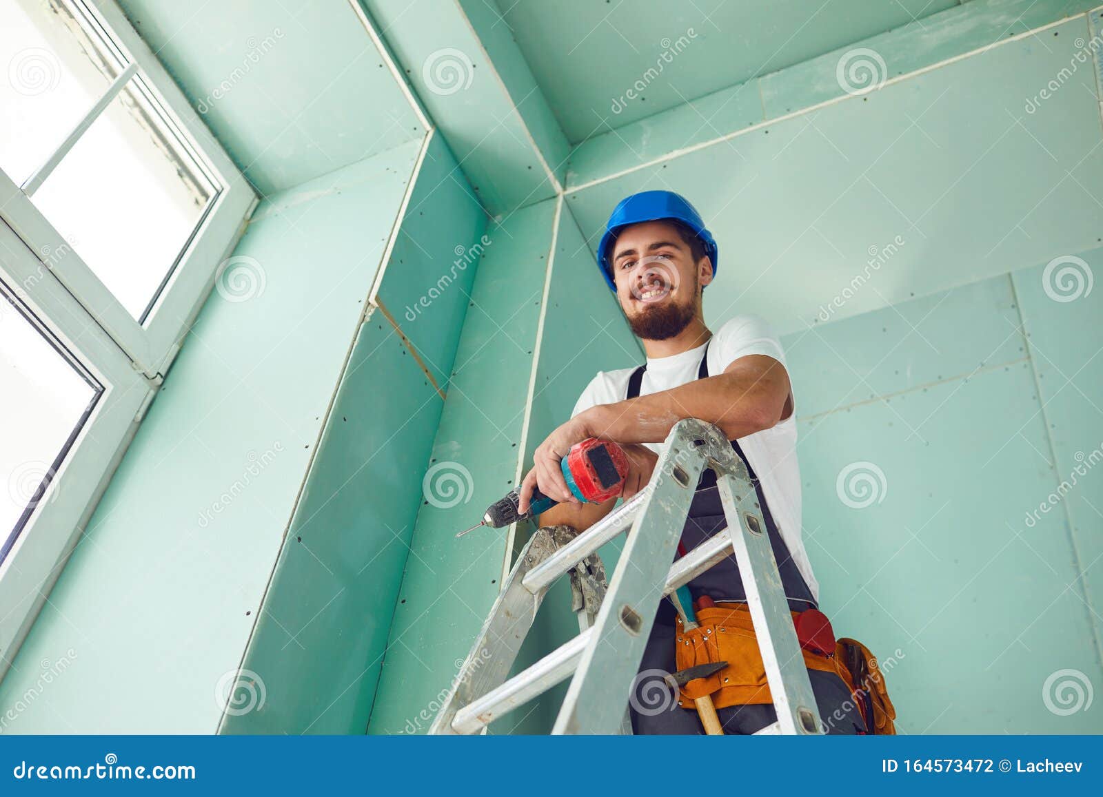 A Builder Standing on a Ladder Installs Drywall at a Construction Site