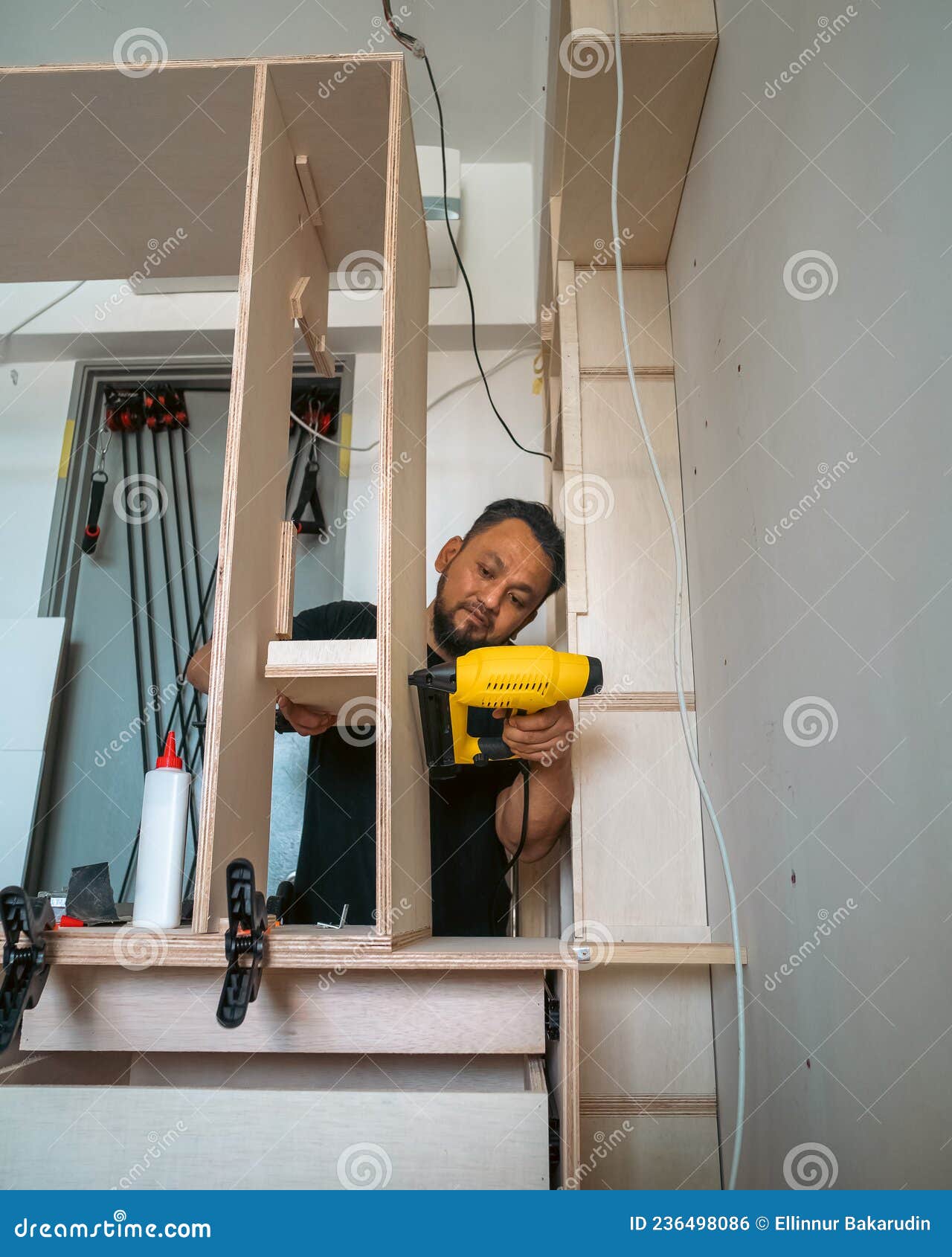 building a wardrobe. man using framing nailer to attach wooden plywoods