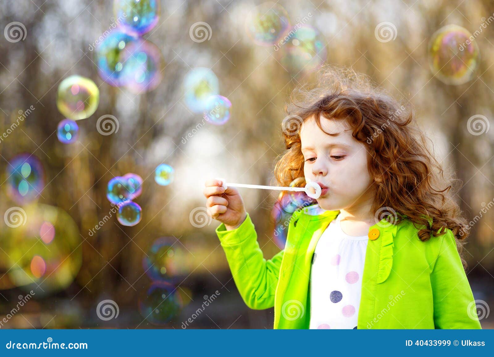 Burbujas de un jabón de la niña que soplan, bebé rizado hermoso del retrato de la primavera
